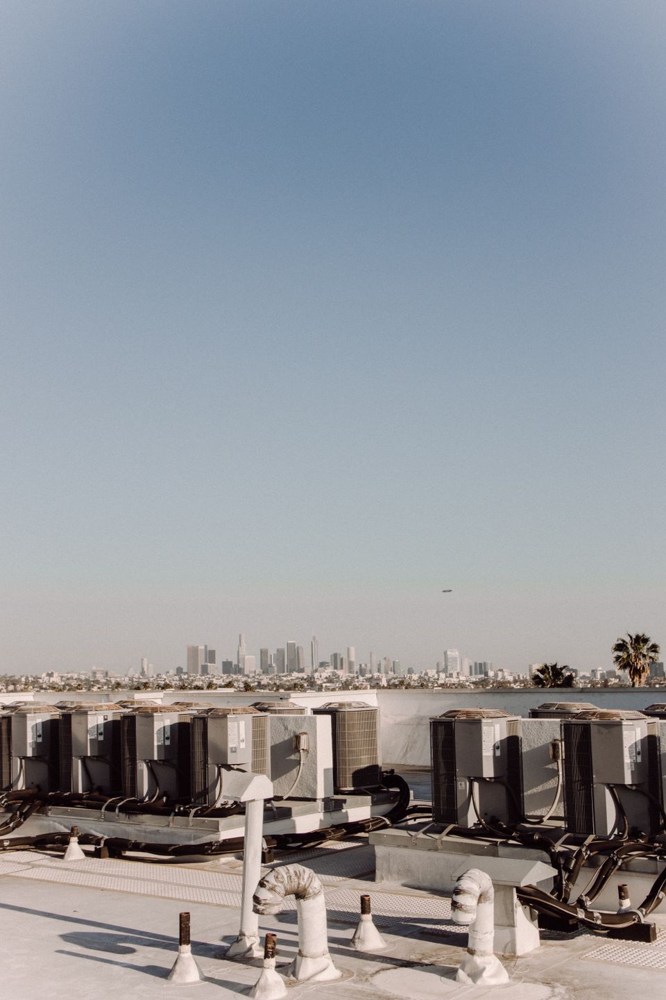Aerial view of rows of commercial HVAC units on a rooftop with a city skyline
