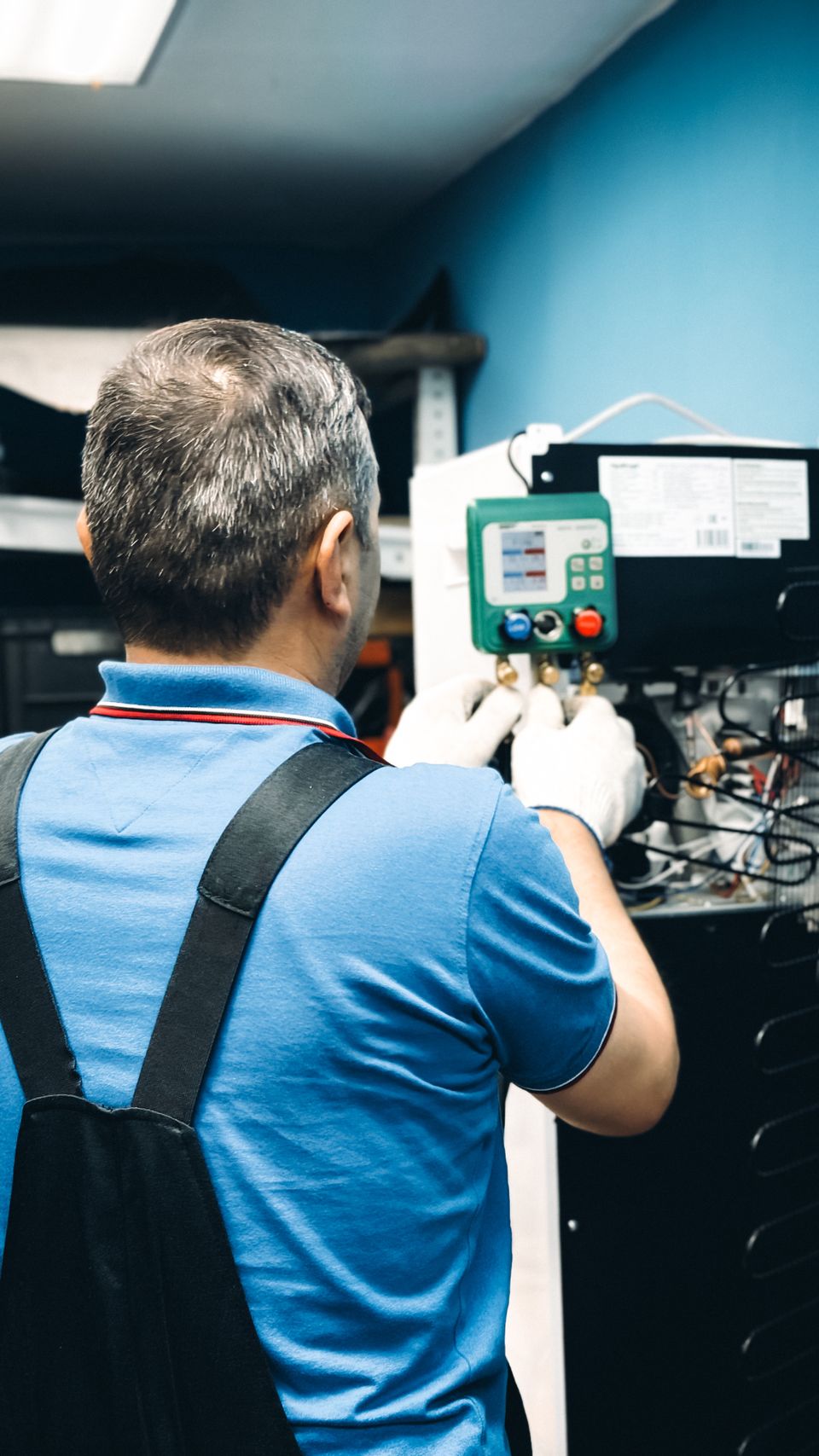 Technician servicing an indoor HVAC unit with refrigerant pressure gauges